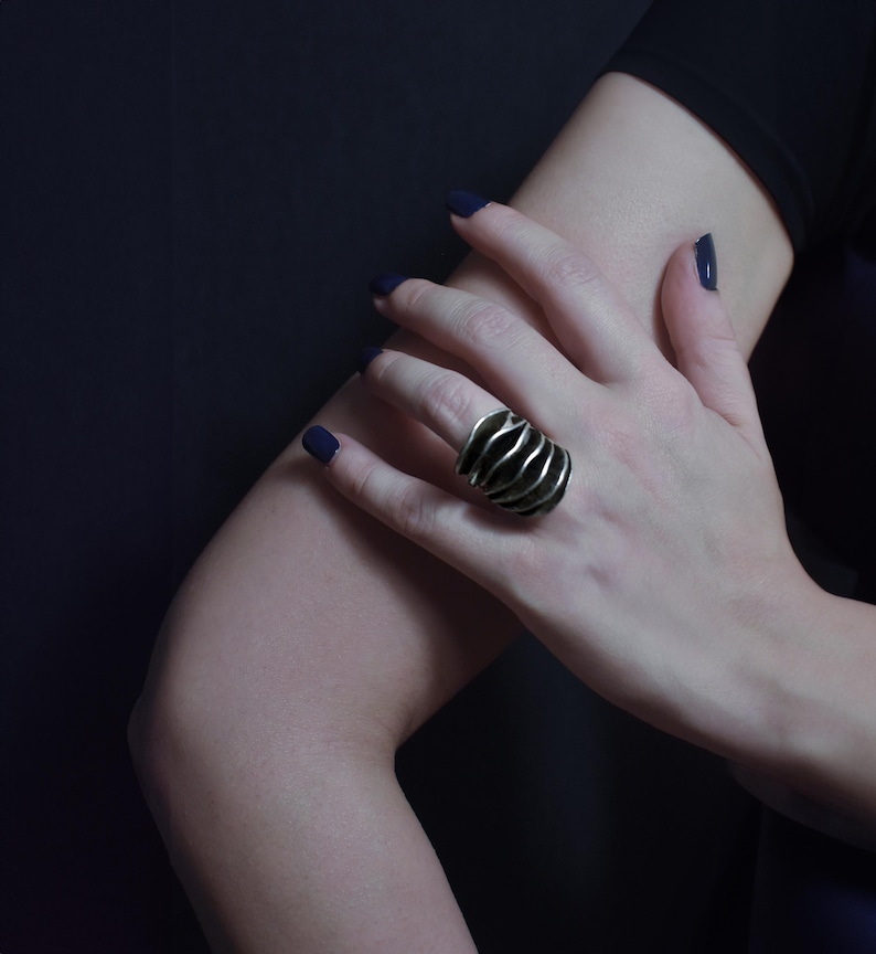 Large Statement silver ring on women's hand resting on her elbow. dark background and elegant styling