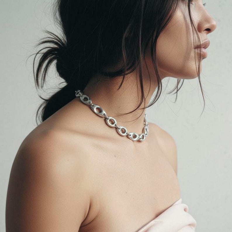 Close-up of a woman wearing a silver sculptural chain necklace with oval open links. The necklace rests along the collarbone, styled with a soft strapless top. Minimal, modern jewelry with an organic industrial design captured in natural light.