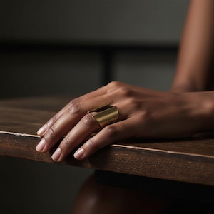 Gold open-band ring with geometric sculptural form worn on hand resting on a wooden table, warm natural lighting and minimalist styling emphasize texture and craftsmanship, modern artisan jewelry by Rannka.