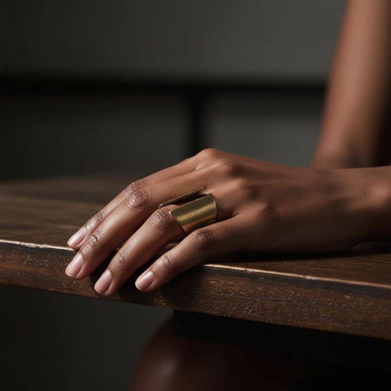 Gold open-band ring with geometric sculptural form worn on hand resting on a wooden table, warm natural lighting and minimalist styling emphasize texture and craftsmanship, modern artisan jewelry by Rannka.