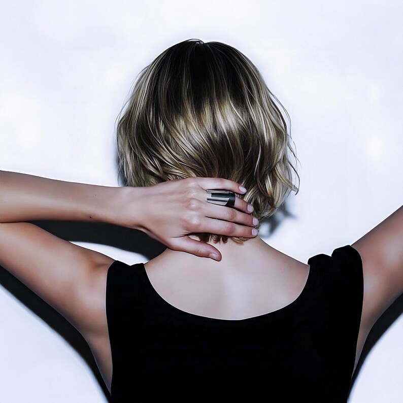 Back view of a woman with short blonde hair wearing a sleeveless black top, her hand resting on her neck adorned with a wide black leather and silver ring. The shot captures a clean, minimalist mood with contemporary styling and soft directional lighting highlighting the jewelry’s sculpted form.
