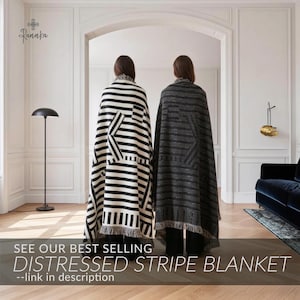 May include: Two individuals draped in distressed stripe blankets. One blanket features black and white stripes with a geometric design, while the other showcases gray stripes. The blankets have fringed edges. Text on the image reads: "SEE OUR BEST SELLING DISTRESSED STRIPE BLANKET --link in description."