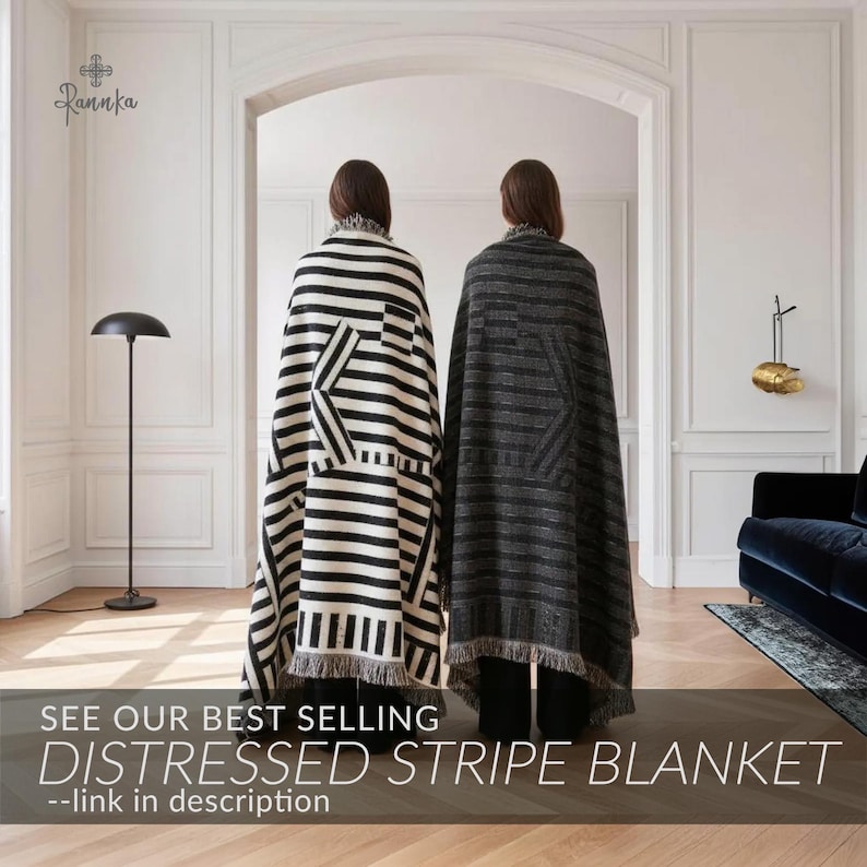 May include: Two individuals draped in distressed stripe blankets. One blanket features black and white stripes with a geometric design, while the other showcases gray stripes. The blankets have fringed edges. Text on the image reads: "SEE OUR BEST SELLING DISTRESSED STRIPE BLANKET --link in description."