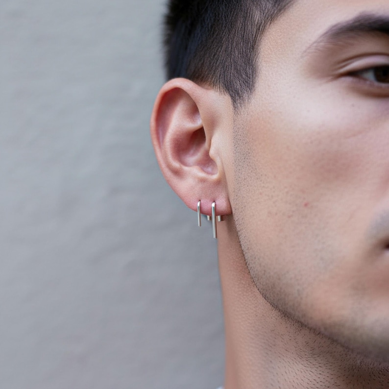 Sterling silver threader earrings worn as a minimal ear stack, thin arc slip earrings in double piercing styling, lightweight pull through earrings, modern curved wire earrings, subtle dangling silver earrings, clean everyday jewelry, close-up ear detail with short hair, sleek contemporary look, Rannka aesthetic