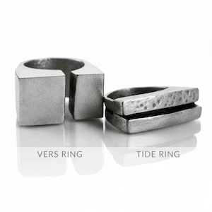 May include: Two silver rings, the "Vers Ring" is a square shape with a gap, and the "Tide Ring" is a layered, rectangular design. Both rings have a matte finish and are displayed on a reflective surface against a white background.