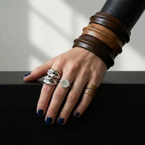 mixed metals and stacked forms on one hand, sculptural silver, flat signet, and warm leather bands layered with carved wooden cuffs, quiet contrast between polished and raw, an easy Rannka moment where materials speak without effort