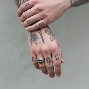 Tattooed hand wearing a geometric silver bar ring with a hammered finish. The ring’s stacked structure adds an industrial edge to the minimalist look. Unisex modern jewelry piece for everyday wear. Rannka handcrafted design.