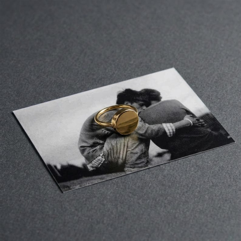 gold signet ring resting over a vintage black and white photograph, memory and object layered into one quiet moment, a subtle Rannka touch where form holds something personal
