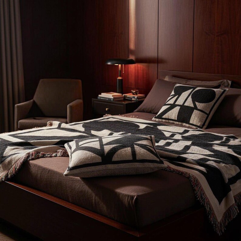 Black and cream woven blanket with geometric patterns and multicolor fringed edges displayed on a neatly made bed with matching pillows. The warm wood-paneled room, soft lighting, and modern decor create a calm, refined atmosphere.