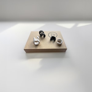 The Black and White Ear Cuffs, an adjustable, no-pierced conch wrap earring style on a jewelry gift box sitting on white surface with soft shadow