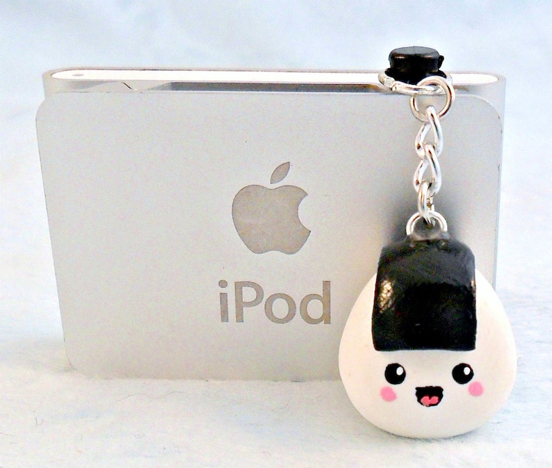 Pu&ograve; includere: Un ciondolo onigiri bianco e nero con un viso sorridente, attaccato a una catena d'argento e un ciondolo nero. Il ciondolo &egrave; appeso a un iPod.