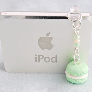 May include: A silver iPod with a white apple logo and the word "iPod" printed on it. A green and white macaron charm hangs from the headphone jack.