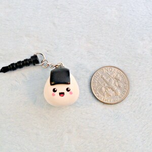 Pu&ograve; includere: Un ciondolo onigiri bianco e nero con un viso carino, attaccato a un jack per cuffie nero.