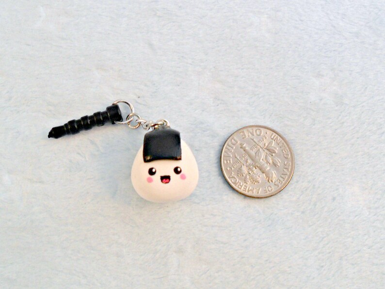 Pu&ograve; includere: Un ciondolo onigiri bianco e nero con un viso carino, attaccato a un jack per cuffie nero.