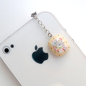 May include: A white phone case with a silver chain attached to a small, white, frosted cookie with colorful sprinkles.
