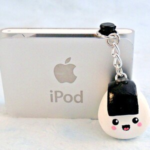 Pu&ograve; includere: Un ciondolo onigiri bianco e nero con un viso sorridente, attaccato a una catena argentata e un ciondolo nero. Il ciondolo &egrave; appeso a un iPod bianco.