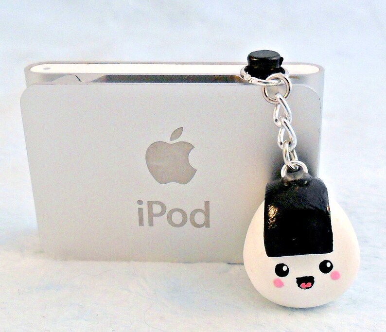 Pu&ograve; includere: Un ciondolo onigiri bianco e nero con un viso sorridente, attaccato a una catena argentata e un ciondolo nero. Il ciondolo &egrave; appeso a un iPod bianco.