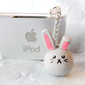 May include: A white iPod with a silver chain attached to a gray bunny charm with pink ears. The bunny has a black nose and whiskers. The iPod has the Apple logo and the word "iPod" printed on it.