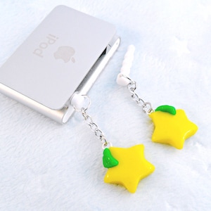 May include: Two yellow star-shaped charms with green leaves dangle from silver chains attached to white earbud plugs. The charms are hanging from a silver iPod.
