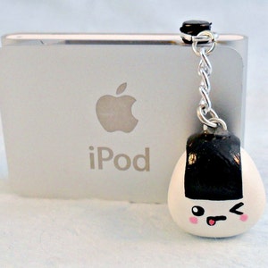 May include: A white and black onigiri charm with a winking face and pink cheeks. The charm is attached to a silver chain and a black clip. The charm is hanging from a silver iPod.