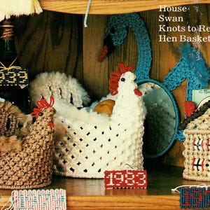 Może przedstawiać: Półka z różnymi przedmiotami wykonanymi na szydełku, w tym domem, łabędziem, koszykiem na kury i butelką z datą 1933. Wszystkie przedmioty są białe z czerwonymi i niebieskimi akcentami. Półka jest drewniana i ma jasnobrązowe wykończenie.