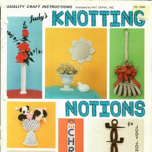 Könnte beinhalten: Ein Vintage-Bastelbuchcover mit dem Titel "Judy's Knotting" und "Notions" mit einem blauen und weißen gehäkelten Design. Das Cover zeigt verschiedene gehäkelte Gegenstände, darunter eine Vase mit Blumen, einen Spiegel, einen Besen, einen Handtuchhalter, ein Namensschild und einen Stiftehalter.