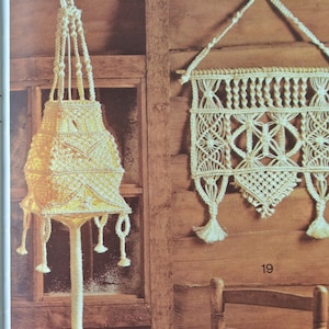 May include: Two macrame wall hangings, one is a lampshade with a white tassel at the bottom and the other is a rectangular wall hanging with a geometric pattern. Both hangings are made with white cord and are displayed against a wooden background.
