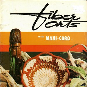 May include: A close-up of a crocheted basket with a white and orange pattern. The basket is made with Maxi-Cord yarn and is sitting on a sandy surface with a wooden branch and a cactus plant. The text "Fiber Arts with Maxi-Cord" is printed on the top of the image.