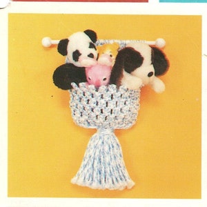 May include: A white crocheted wall hanging with a blue and white tassel. The hanging has a woven basket shape and is filled with stuffed animals, including a panda, a pig, and a dog.