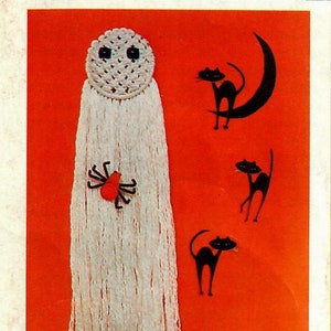Puede incluir: Un fantasma blanco de crochet con ojos negros y una araña roja colgando de él. Hay tres gatos negros y una luna creciente sobre un fondo naranja. Una vela y una tarjeta que dice "¡Feliz Halloween!" están en la esquina inferior derecha.