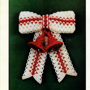 May include: A white and red crocheted bow with two red bells hanging from the center. The bow is a traditional Christmas decoration.
