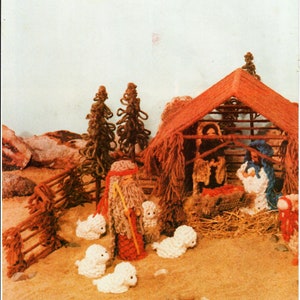 以下が含まれることがあります： 手作りの降誕シーン。小屋、人物、羊が特徴です。人物には杖を持った男性や、赤、青、白の人物が含まれます。シーンは砂地の表面に設定され、木の柵と茶色の木があります。