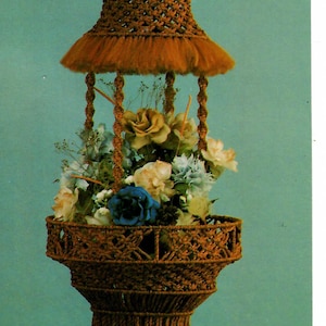 May include: A brown macrame hanging planter with a fringe bottom and a flower pot filled with colorful flowers. The planter is hanging from a ceiling or wall.