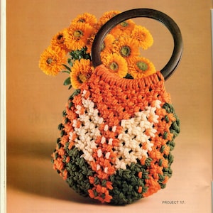Op de afbeelding: Een gehaakte tas met een houten handvat. De tas is gemaakt van oranje, groen en wit garen. De tas staat op een tafel met een boeket oranje bloemen.