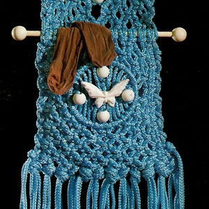 May include: A blue macrame wall hanging with white butterflies and wooden dowels. The hanging has a fringe at the bottom.