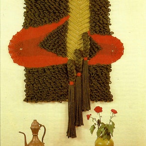 Peut inclure: Une tapisserie murale en macramé de couleur marron, verte et rouge avec des glands. La tapisserie murale est accrochée à un mur jaune clair. Au premier plan, il y a un vase avec des fleurs rouges sur une table en bois.