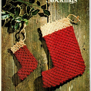 May include: Two red and white crocheted Christmas stockings hanging on a wooden background. The larger stocking has a tan top and the smaller stocking has a tan cuff.