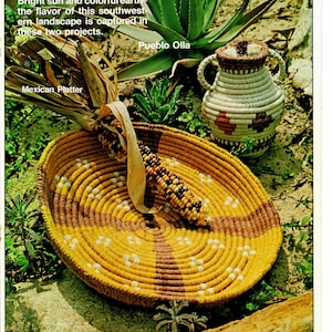 Puede incluir: Dos cestas tejidas, una Pueblo Olla y un plato mexicano, se muestran sobre una superficie rocosa con plantas verdes. La Pueblo Olla es una cesta pequeña y redonda con un patrón marrón, blanco y naranja. El plato mexicano es una cesta redonda más grande con un patrón amarillo, marrón y blanco. Una mazorca de maíz seca descansa dentro del plato mexicano.