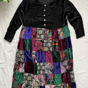 May include: A vintage dress with a black velvet bodice and long sleeves. The skirt is a patchwork of jewel-toned velvet and floral fabrics. The dress has a scoop neckline and is buttoned down the front with iridescent buttons. The tag reads "Shirley D".