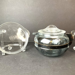 May include: A clear glass teapot with a black band around the middle and a clear glass lid. The teapot has a clear glass handle and a matching clear glass base.