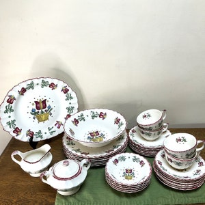 May include: A set of white ceramic dinnerware with a floral pattern featuring red, green, and yellow accents. The set includes plates, bowls, and cups.