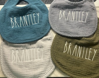 May include: Four baby bibs with the name "Brantley" embroidered in white on each. The bibs are in different colors: teal, gray, light gray, and olive green.