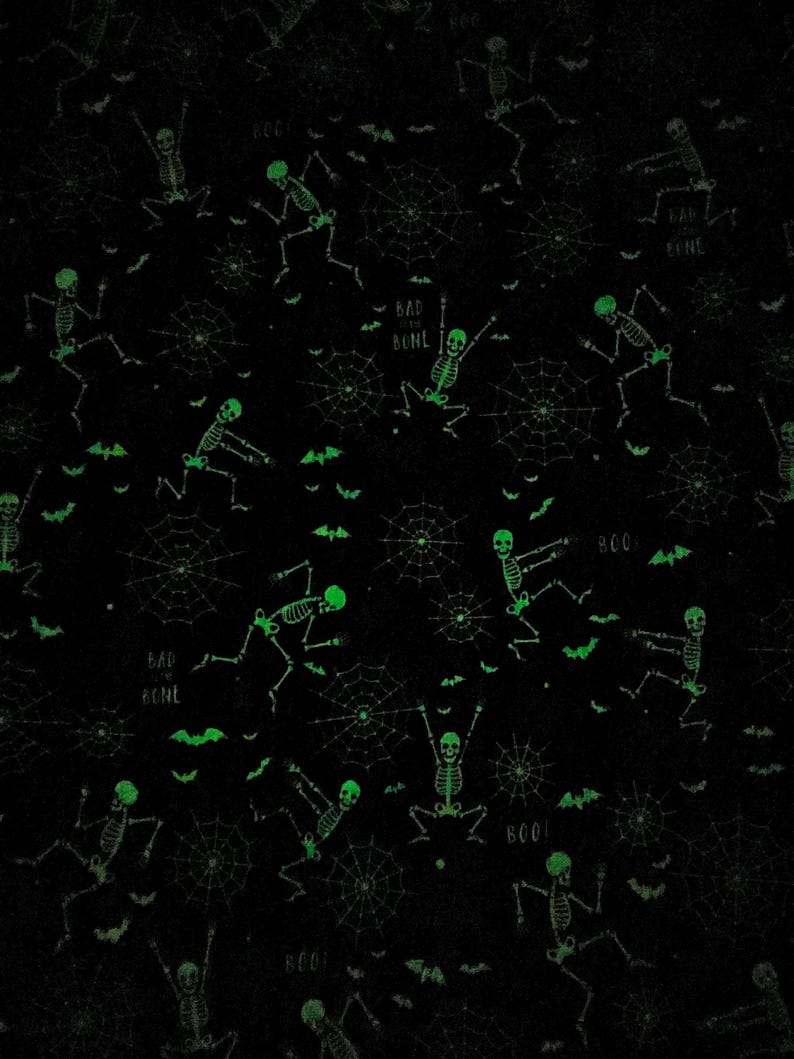 May include: Black fabric with a repeating pattern of glowing green skeletons in various poses, spiderwebs, and bat silhouettes. The words "BAD BONE" and "BOO!" are also scattered across the design. This Halloween-themed fabric is suitable for various craft projects.