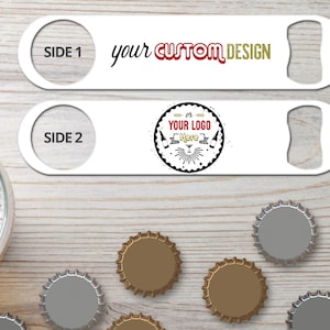 May include: Two white metal bottle openers with a bottle opener on one end and a round hole on the other end. The top opener has the text 'SIDE 1 your CUSTOM DESIGN' and the bottom opener has the text 'SIDE 2 or YOUR LOGO Here'. The openers are on a woodgrain surface with several bottle caps.