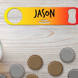 Puede incluir: Un abridor de botellas de metal amarillo y rojo con el nombre "JASON" impreso en él. El abridor de botellas está sobre una superficie de madera con varias tapas de botellas esparcidas a su alrededor.