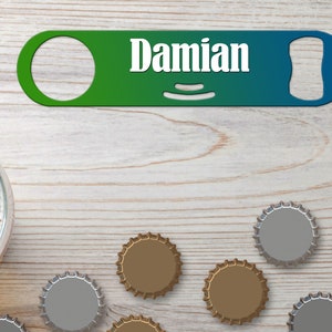 Puede incluir: Un abridor de botellas verde y azul con la palabra "Damian" impresa en él. El abridor de botellas está sobre una superficie de madera con varias tapas de botellas.
