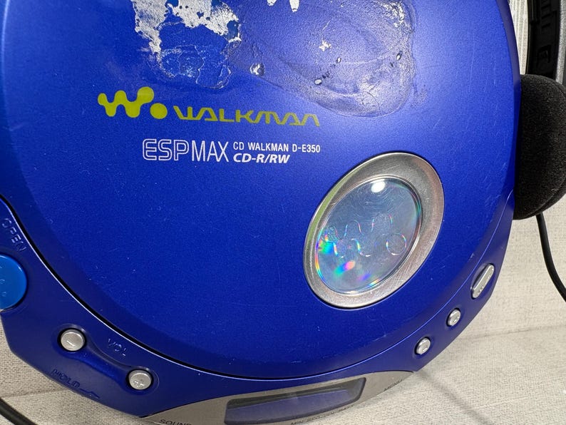 May include: A blue portable CD player with a circular design. The device features the Walkman logo, ESP MAX, and CD Walkman D-E350 CD-R/RW text printed on the top surface. It includes a small circular window, control buttons, and a blue open switch.