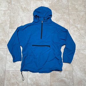 May include: A blue hooded pullover jacket with a half-zip closure and a kangaroo pocket. The jacket has a drawstring at the bottom.