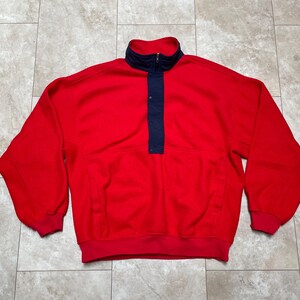 Könnte beinhalten: Roter Fleece-Pullover mit einem dunkelblauen Stehkragen und einem einzigen Knopfverschluss.