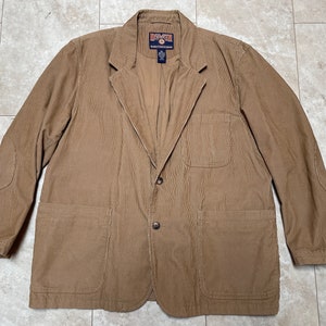 May include: A tan corduroy blazer with a notched lapel, two front pockets, and elbow patches. The blazer has a two-button closure and a label on the chest. The jacket is a classic style.